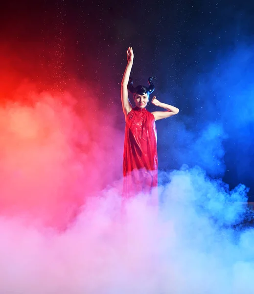 beautiful woman in red dress of the goddess of the earth in smoke dancing in the rain