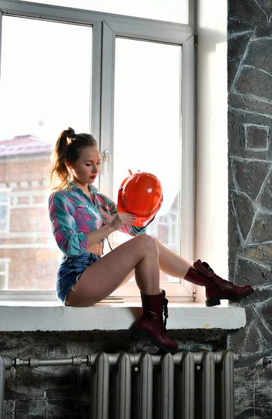 制服を着て窓からオレンジのヘルメットを守る美しい女の子 — ストック写真