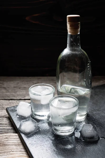 Vista close-up de vodka garrafa com óculos de pé no gelo preto — Fotografia de Stock