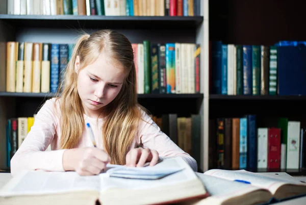 Écolière étudiant avec des manuels tout en écrivant sur un livre — Photo