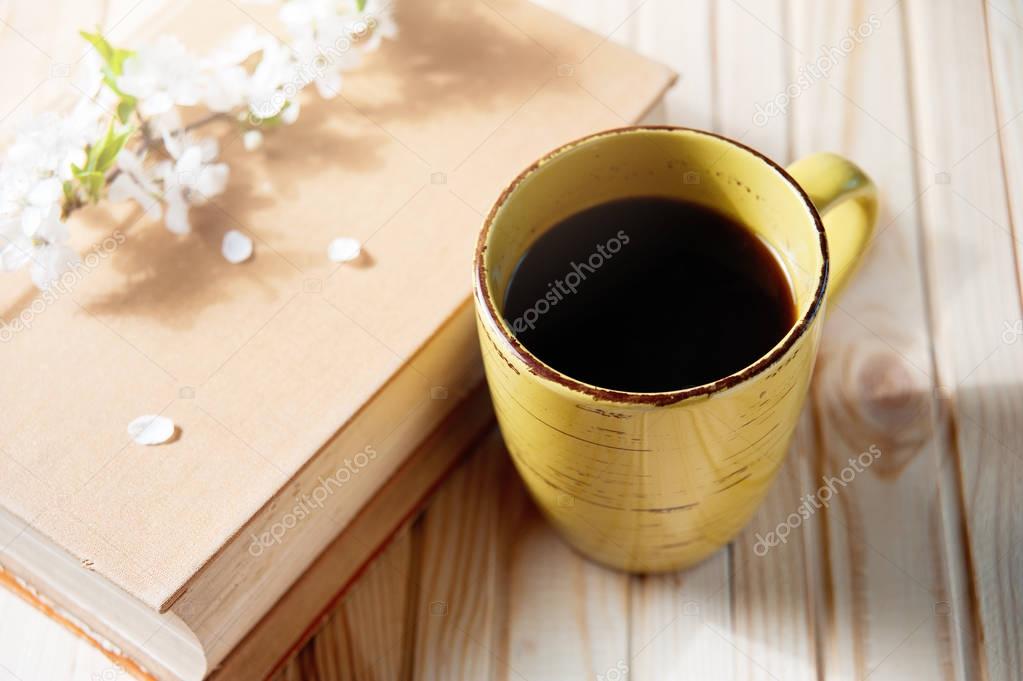 old book, cup of coffee next to spring white flowers on wooden texture