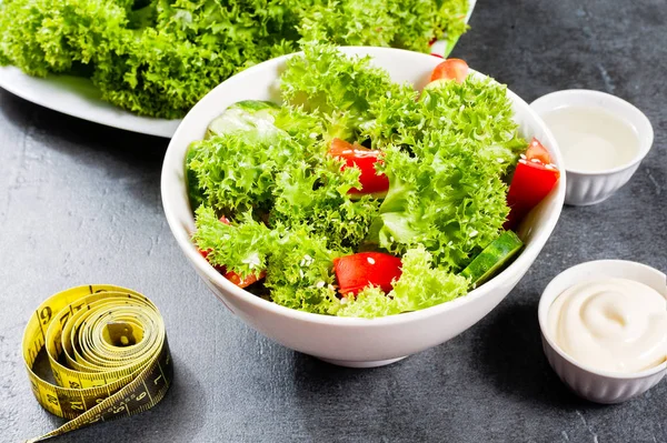 Diet plan - salad of fresh vegetables and tape measure on dark stone table