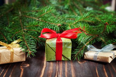 Köknar dallarında yapılan bir çerçeve içinde ahşap arka plan üzerinde kırmızı kurdele ile Noel hediyeleri.
