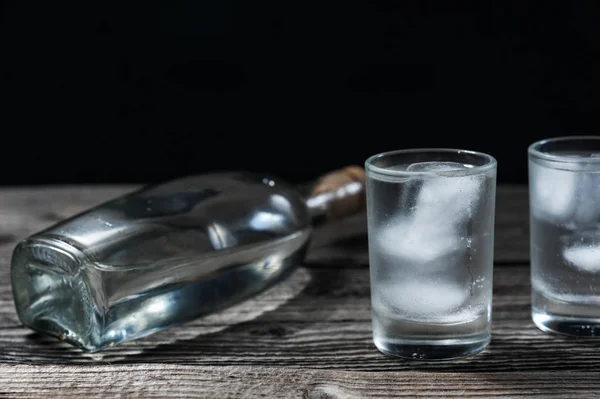 Vodka v zastřelených glassesand láhev na rustikální dřevo stůl černé pozadí — Stock fotografie