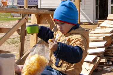 Pikniğe giden çocuk sokakta mısır yiyip çay içiyor.