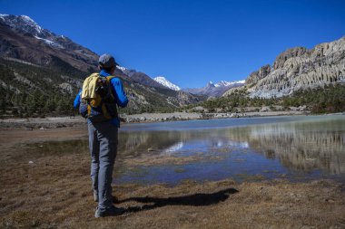 Kar dağları sırtında gölün manzarasına bakmak için ayakta duran adam