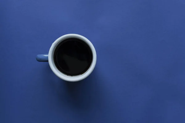 Cup of coffee on blue paper background, dark blue tones image — Stock Photo, Image