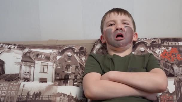 Malheureux garçon assis sur le canapé et Hamming, bras croisés, peinture faciale — Video
