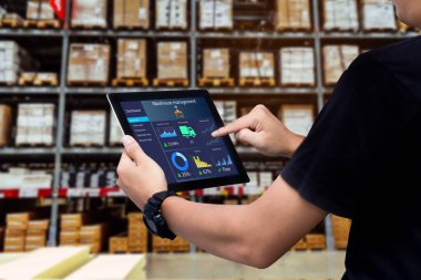 Akıllı depo yönetim sistemi. İşçi elleri arka plan olarak bulanık depoda tablet tutuyor.