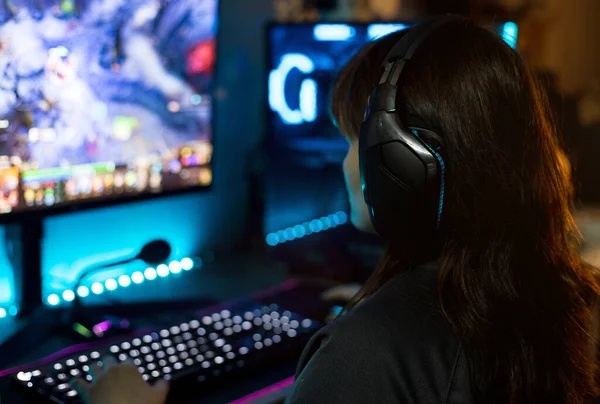 Back view of young female gamer playing video games at home