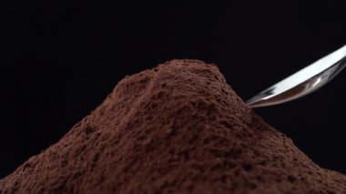 Siyah arka planda izole edilmiş küçük bir kaşık ile kakao tozu dozajı yavaş çekimde
