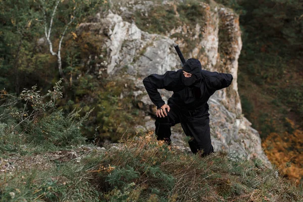 The assassin ninja sword crouched on cliff rocks in ambush