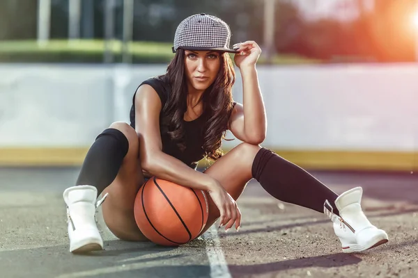 Beautiful brunette woman playing basketball on court outdoor sunset.
