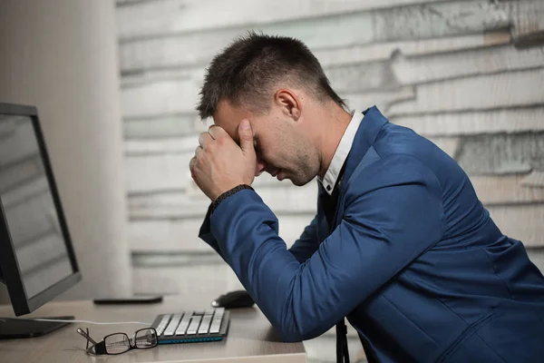 Tired business man at workplace in office holding his head on hands. Sleepy worker early in the morning after late night work. Overworking, making mistake, stress, termination or depression concept