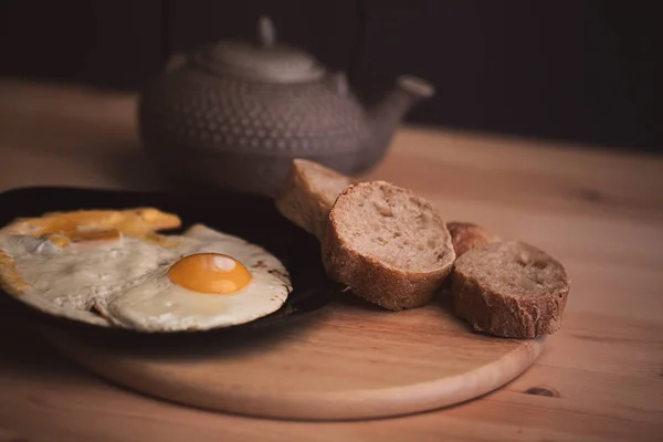 Huevos revueltos con pan de centeno sobre una mesa de madera. Tetera de cerámica japonesa en el fondo. Fotos de comida en un estilo contemporáneo y tonificación —  Fotos de Stock