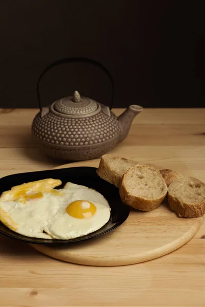 黑麦面包木制的桌子上西红柿炒鸡蛋。日本陶瓷茶壶在背景中。照片在当代的食物风格和色调 — 图库照片
