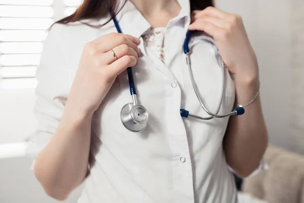 Een jonge vrouwelijke dokter in een witte Kiel houden een stethoscoop in armen op de nek. Onscherpe achtergrond. Concept van medische hulp. — Stockfoto