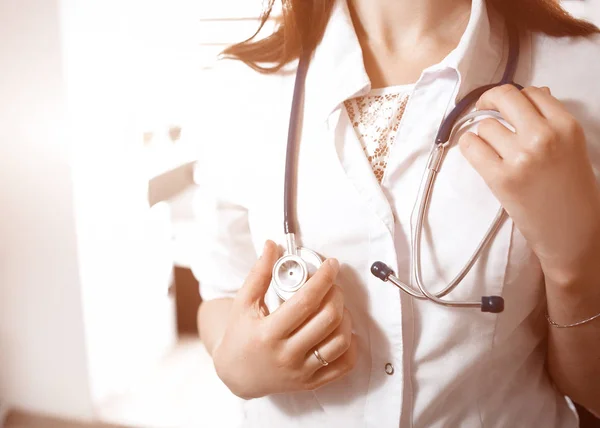 Seorang dokter wanita muda dengan baju putih memegang stetoskop di leher. Latar belakang kabur. Konsep bantuan medis . — Stok Foto