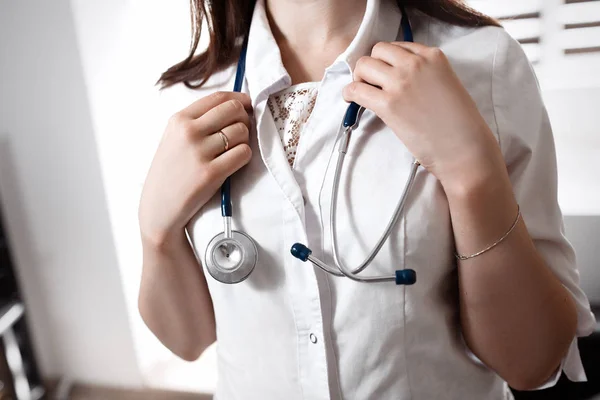 Mladá lékařka v bílé zástěře drží v náručí na krku stetoskop. Rozmazané pozadí. Koncept lékařskou pomoc. — Stock fotografie