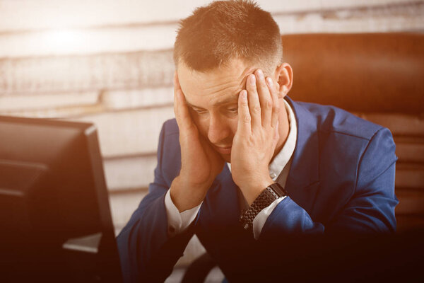 Уставший бизнесмен на рабочем месте в офисе держит голову на ха
