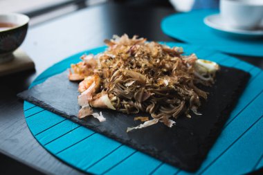 Buğday noodle ile karides ve talaşı ton balığı soslu siyah plaka üzerinde. Asya gıda arka plan. Beslenme kavramı. Ahşap masa ile restoran yer. İşaret fişeği kopya alanı için metin, tasarım