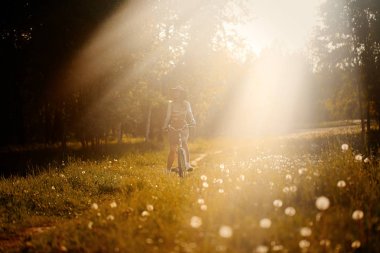 Komik kız sürüş Bisiklet açık. Güneşli yaz yaşam tarzı kavramı. Kadın elbise ve şapka alanında dandelions. Kadın araba park. Metin ışık fotoğraf efekti. Boşaltmak için tasarım.
