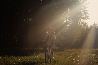 Komik kız sürüş Bisiklet açık. Güneşli yaz yaşam tarzı kavramı. Kadın elbise ve şapka alanında dandelions. Kadın araba park. Metin ışık fotoğraf efekti. Boşaltmak için tasarım.