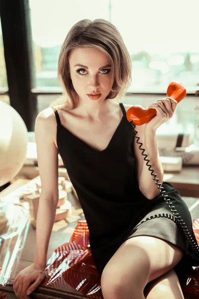Närbild porträtt av en vacker ung kvinna med retro röd telefon sitter på bord. Flicka med naken make up, mode ögonbryn och gröna ögon. Skönhet-konceptet. Vintage stil — Stockfoto