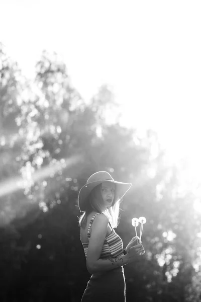 Силуэт девушки, гуляющей в парке под открытым небом. Солнечный летний образ жизни. Женщина в платье и шляпа в поле с одуванчиками. Эффект свечения текста. Копирайт для дизайна. BW фото . — стоковое фото