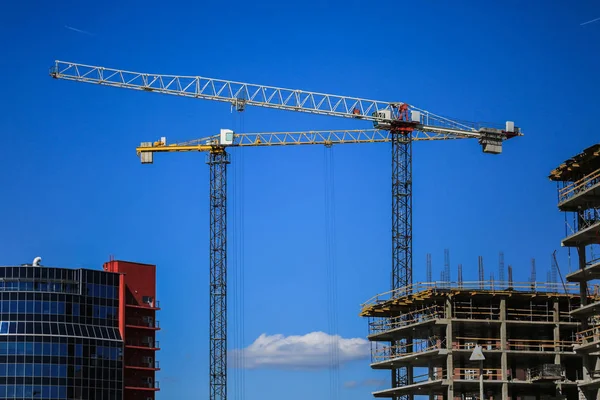 Baukonzept. ein neues Gebäude im Bau gegen den Himmel. blauer Hintergrund. Neue urbane Stadt. Maschinen, Kräne und Bauarbeiter auf Gerüsten. Schwerindustrie und Arbeitssicherheit — Stockfoto