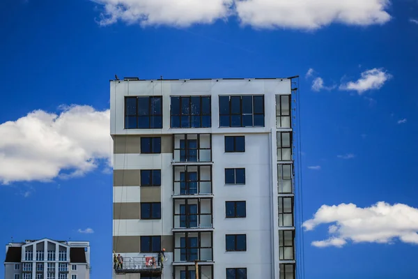 Konstruktion koncept. En ny byggnad under uppförande mot himlen. Blå bakgrund. Nya urbana staden. Maskiner, kranar och byggare på byggnadsställningar. Tung industri och säkerhet på arbetsplatsen — Stockfoto