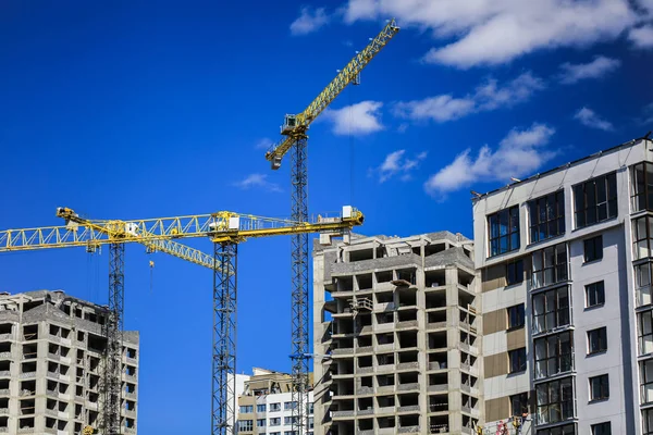 Baukonzept. ein neues Gebäude im Bau gegen den Himmel. blauer Hintergrund. Neue urbane Stadt. Maschinen, Kräne und Bauarbeiter auf Gerüsten. Schwerindustrie und Arbeitssicherheit — Stockfoto