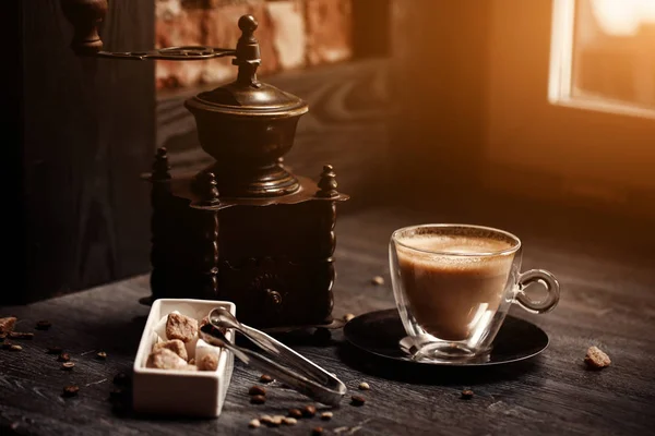 Taza de café en la cafetería de color vintage. Molinillo de café y azúcar de caña marrón en la mesa de madera con fondo borroso llamarada. Estilo retro — Foto de Stock