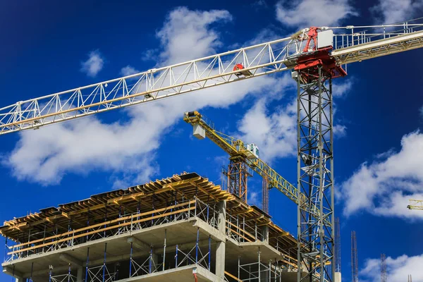 Baukonzept. ein neues Gebäude im Bau gegen den Himmel. blauer Hintergrund. Neue urbane Stadt. Maschinen, Kräne und Bauarbeiter auf Gerüsten. Schwerindustrie und Arbeitssicherheit — Stockfoto