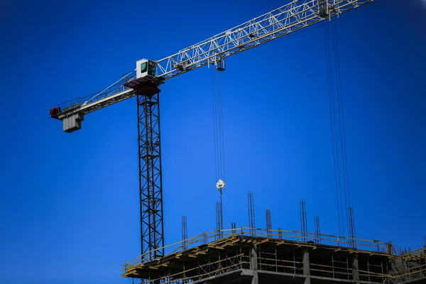 Construction concept. A new building under construction against the sky. Blue background. New urban city. Machinery, cranes and builders on scaffolding. Heavy industry and safety at work — Stock Photo, Image