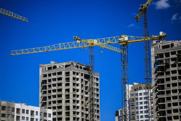 Baukonzept. ein neues Gebäude im Bau gegen den Himmel. blauer Hintergrund. Neue urbane Stadt. Maschinen, Kräne und Bauarbeiter auf Gerüsten. Schwerindustrie und Arbeitssicherheit — Stockfoto