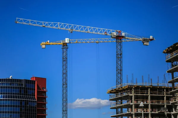 Construction concept. A new building under construction against the sky. Blue background. New urban city. Machinery, cranes and builders on scaffolding. Heavy industry and safety at work
