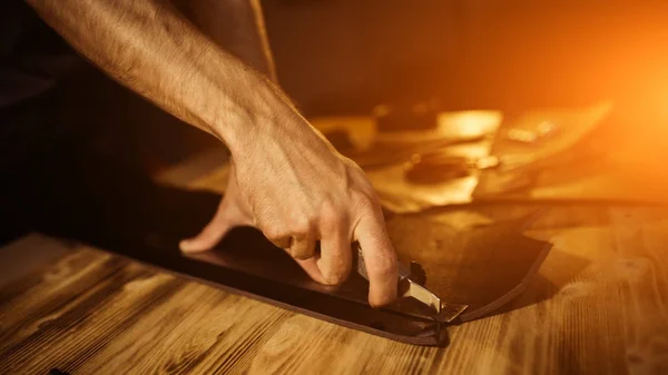 Arbeitsprozess des Ledergürtels in der Lederwerkstatt. Mann hält Werkzeug. Gerber in der alten Gerberei. Holztischhintergrund. Nahaufnahme Mann Arm. warmes Licht für Text und Design. Größe der Web-Banner — Stockfoto