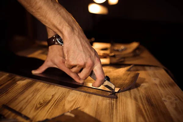 Werkproces van de lederen riem in de workshop leer. Man bedrijf crafting tool en werken. Tanner in oude leerlooierij. Houten tafel achtergrond. Close-up van man-arm — Stockfoto