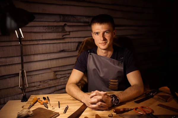 Processus de travail de la ceinture en cuir dans l'atelier de cuir. Homme tenant la main sur une table en bois. Outils d'artisanat sur fond. Tanner dans une vieille tannerie. Fermez le bras des hommes. Interverrouiller les doigts — Photo