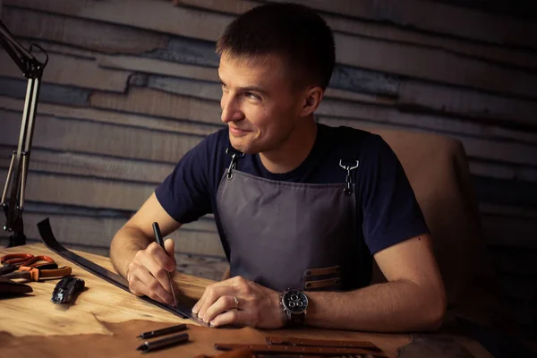 Arbeitsprozess des Ledergürtels in der Lederwerkstatt. Mann hält Werkzeug in der Hand und arbeitet. Gerber in der alten Gerberei. Holztischhintergrund. Nahaufnahme Mann Arm — Stockfoto