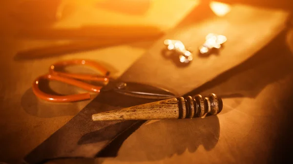 Proceso de trabajo del cinturón de cuero en el taller de cuero. Tanner en curtiduría vieja. Herramienta de elaboración sobre fondo de tabla de madera. Luz cálida para texto y diseño . — Foto de Stock