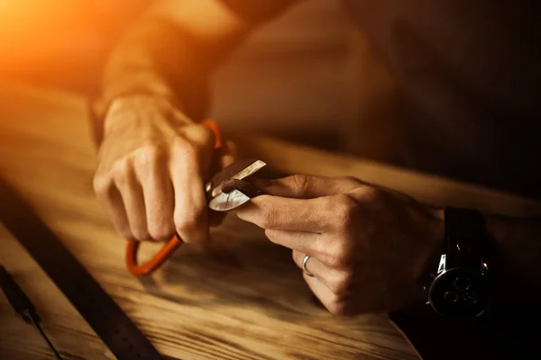 Arbeitsprozess des Ledergürtels in der Lederwerkstatt. Mann hält Werkzeug in der Hand und arbeitet. Gerber in der alten Gerberei. Holztischhintergrund. Nahaufnahme Mann Arm. warmes Licht für Text und Design — Stockfoto