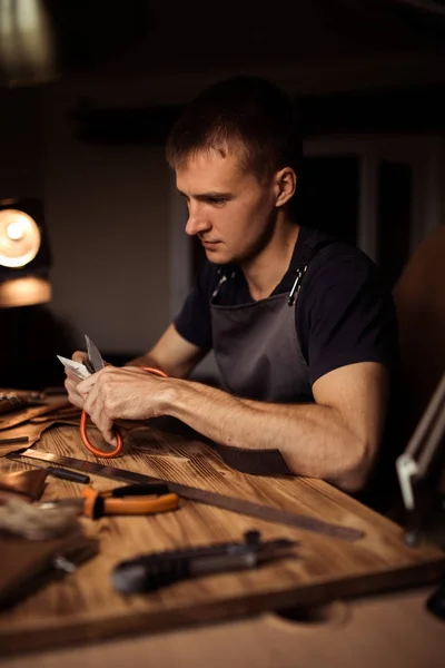 Werkproces van de lederen riem in de workshop leer. Man bedrijf crafting tool en werken. Tanner in oude leerlooierij. Houten tafel achtergrond. Close-up van man-arm — Stockfoto