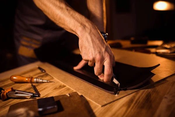 Arbeitsprozess des Ledergürtels in der Lederwerkstatt. Mann hält Werkzeug in der Hand und arbeitet. Gerber in der alten Gerberei. Holztisch Hintergrund — Stockfoto