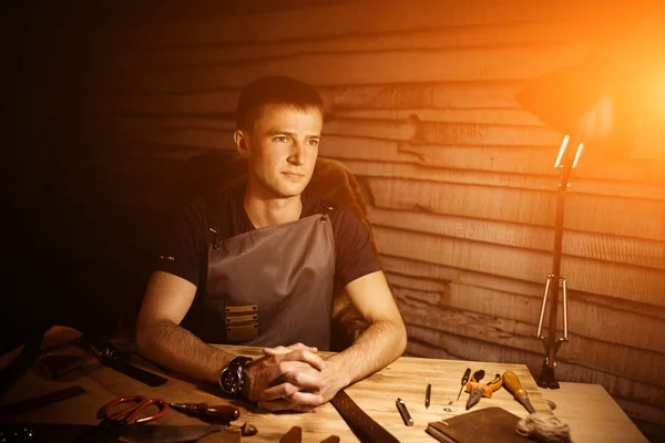 Arbeitsprozess des Ledergürtels in der Lederwerkstatt. Mann hält Hände auf Holztisch. Bastelwerkzeuge im Hintergrund. Gerber in der alten Gerberei. warmes Licht für Text und Design. — Stockfoto