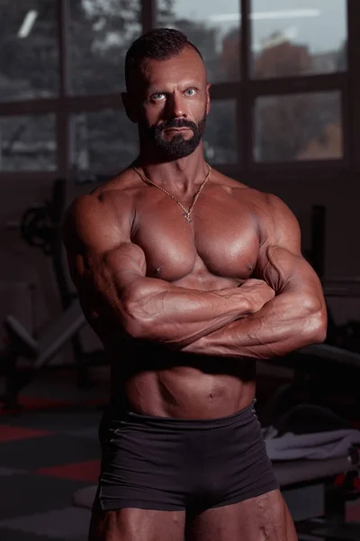 Sportsman in gym. Muscular athletic man standing near barbell. Brutal male with tanned skin and muscle torso. Closeup vertical shot of bodybuilder. No excuses in sports. — Stock Photo, Image