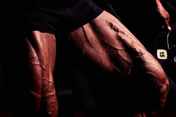 Αθλητής στο γυμναστήριο. Ο τύπος κάνει ασκήσεις. Πορτραίτο closeup των ποδιών με τις φλέβες. Αρσενικό μοντέλο με μαυρισμένο δέρμα. Σέξι άντρας bodybuilder στέκεται με barbell. — Φωτογραφία Αρχείου