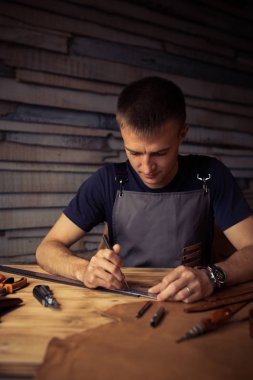 Working process of the leather belt in the leather workshop. Man holding crafting tool and working. Tanner in old tannery. Wooden table background. Close up man arm clipart
