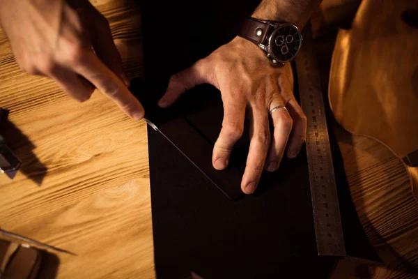 Arbeitsprozess des Ledergürtels in der Lederwerkstatt. Mann hält Werkzeug in der Hand und arbeitet. Gerber in der alten Gerberei. Holztisch Hintergrund — Stockfoto